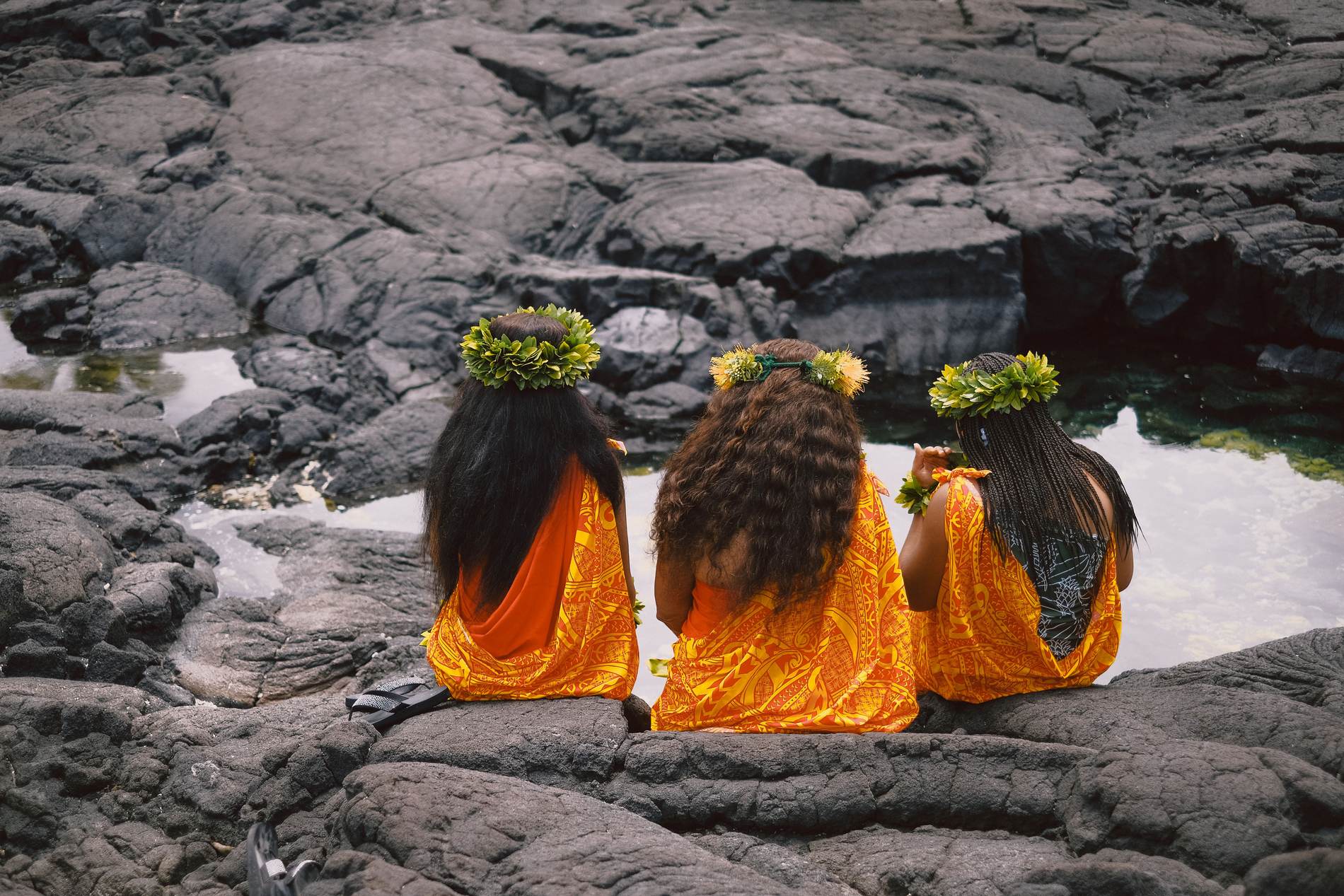 Three women seated quietly above a tide pool on the lava