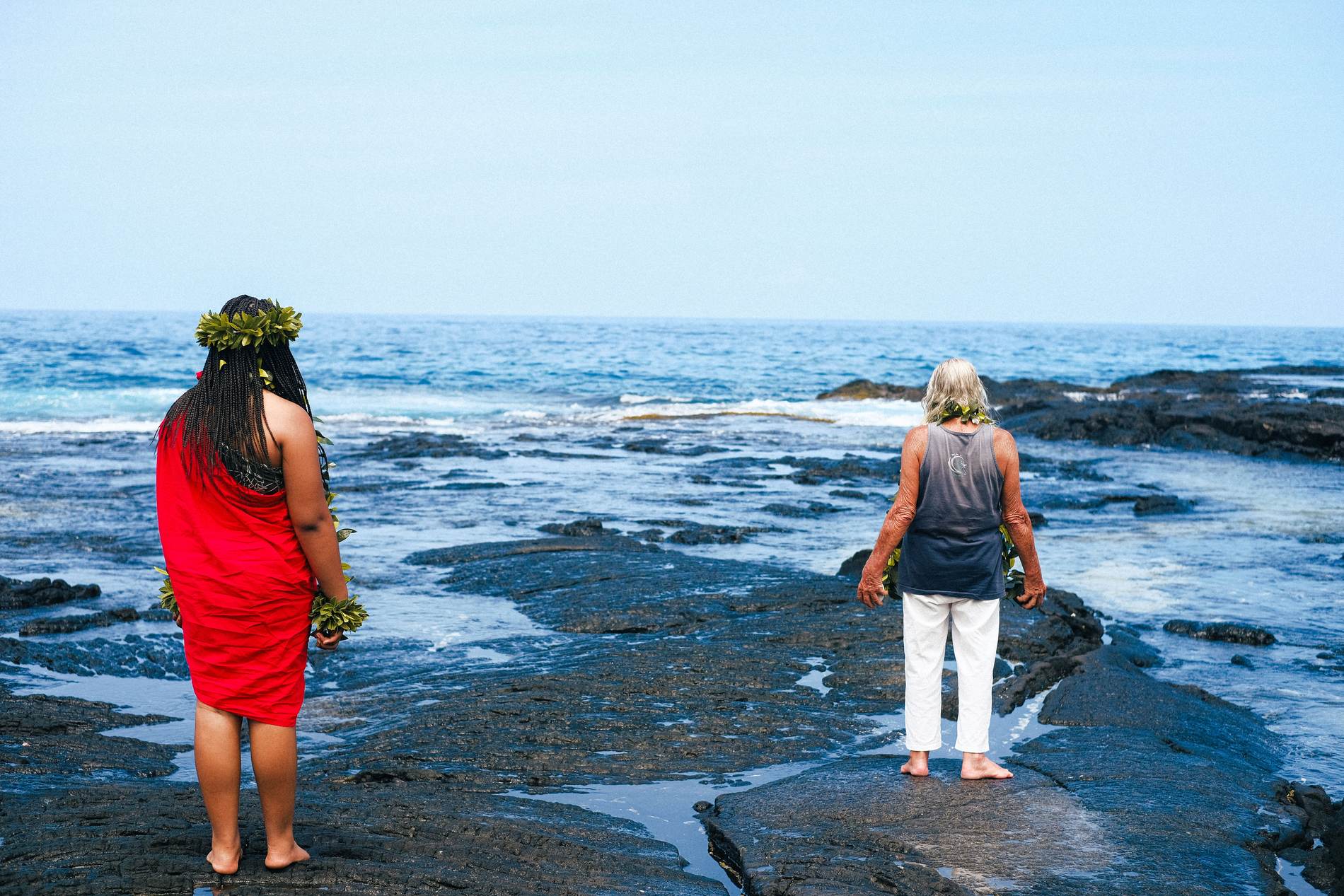 Two figures at the water's edge on the lava shore