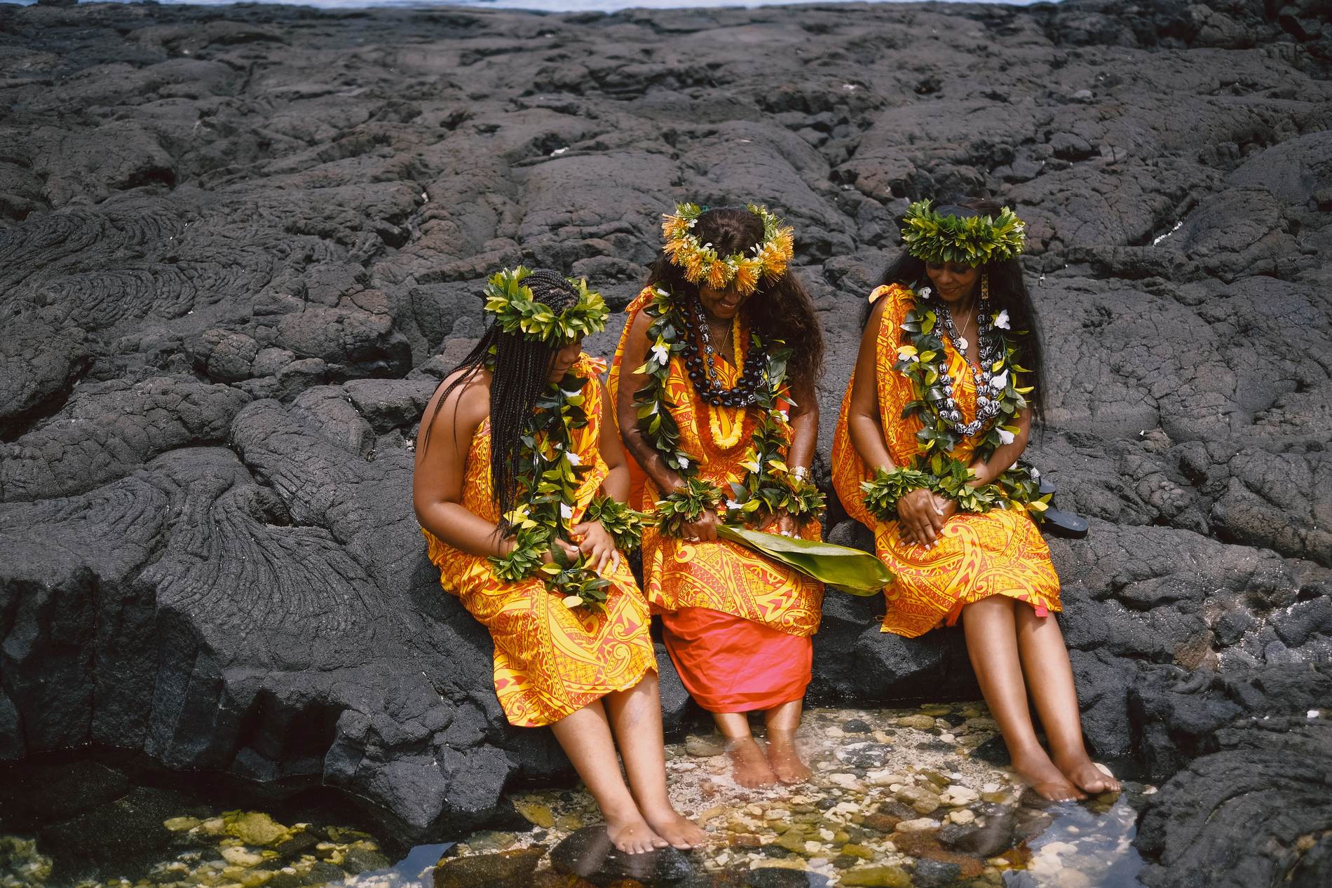 Kahu Kāhealani with her daughter and granddaughter seated together beside a tide pool