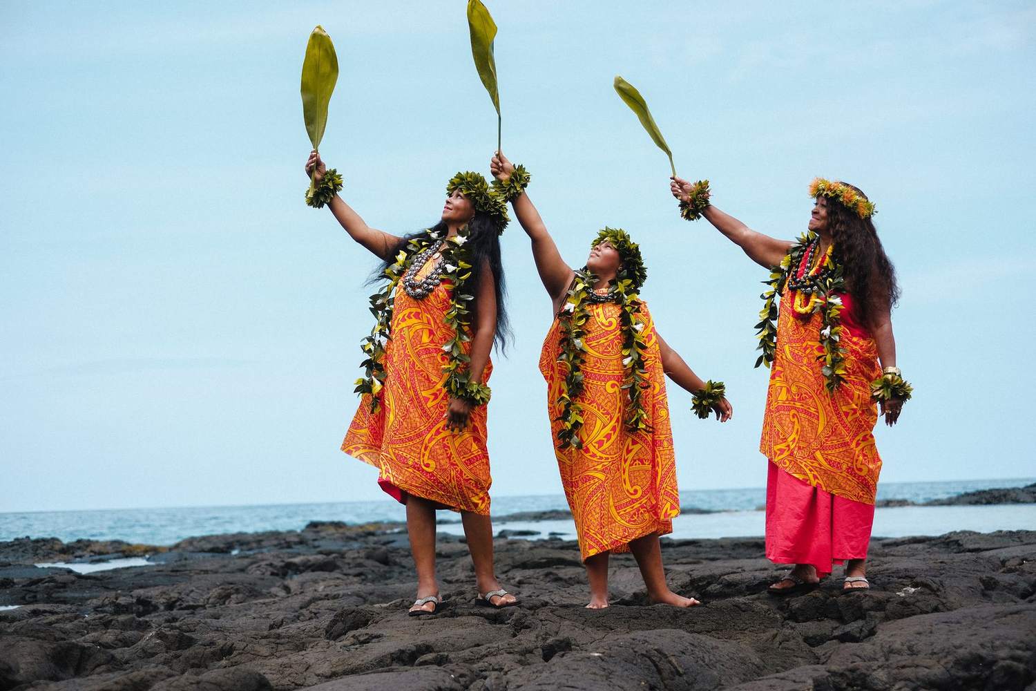 Three generations with ti leaves raised on the lava shore